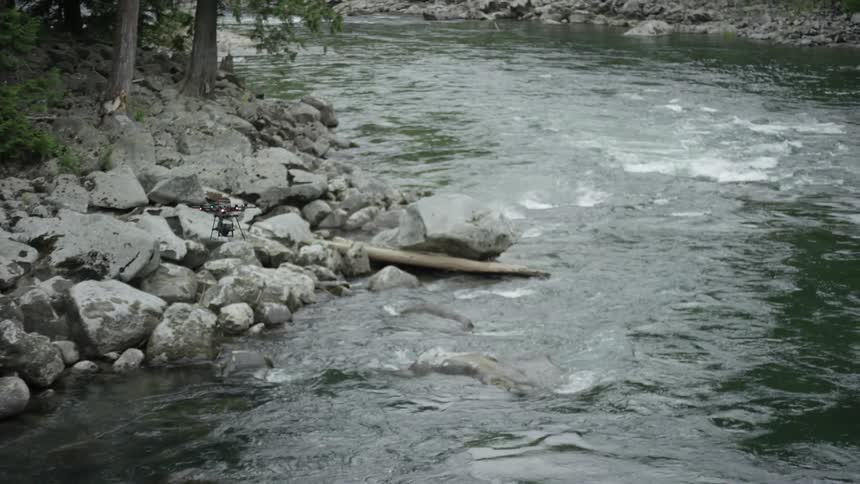 A drone flies over a rocky river in a forest during the day