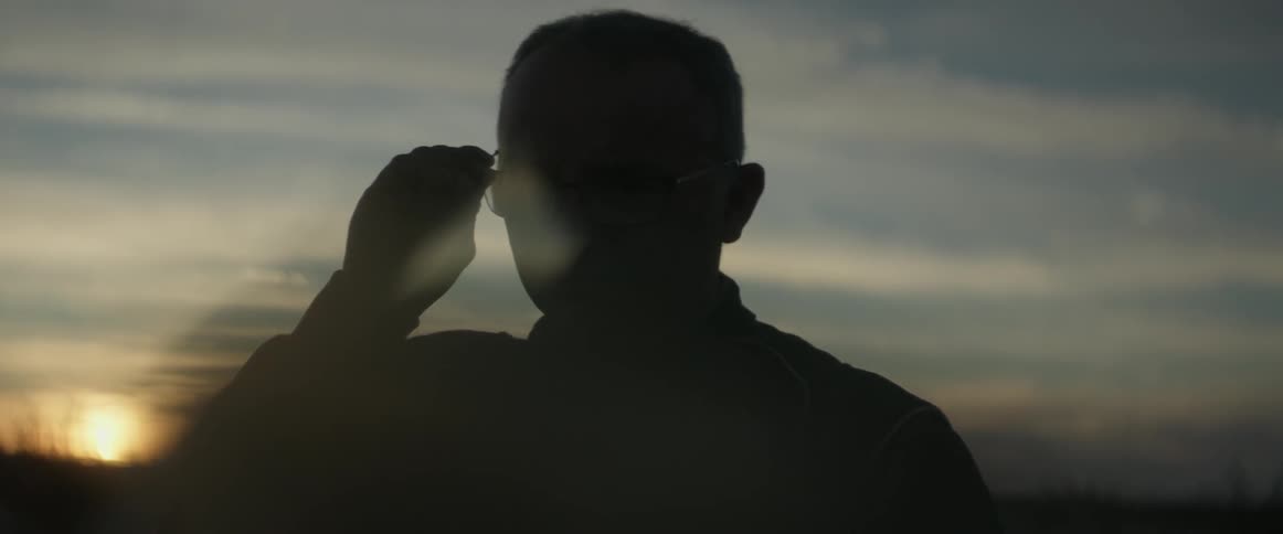 Man puts glasses on outside at sunset