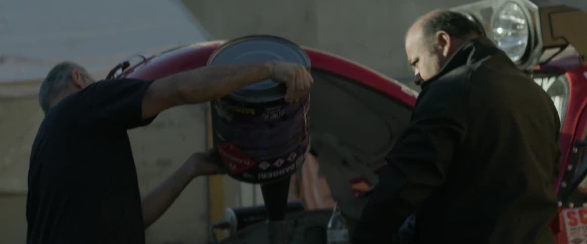 A man pours fluid into an open car hood