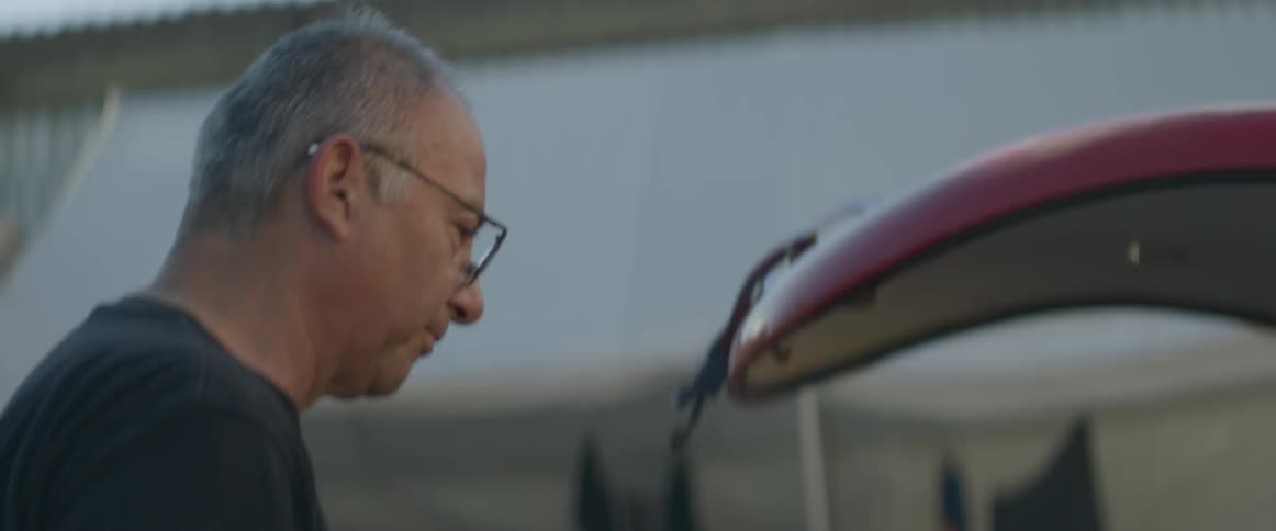 A man bends down looking inside a car