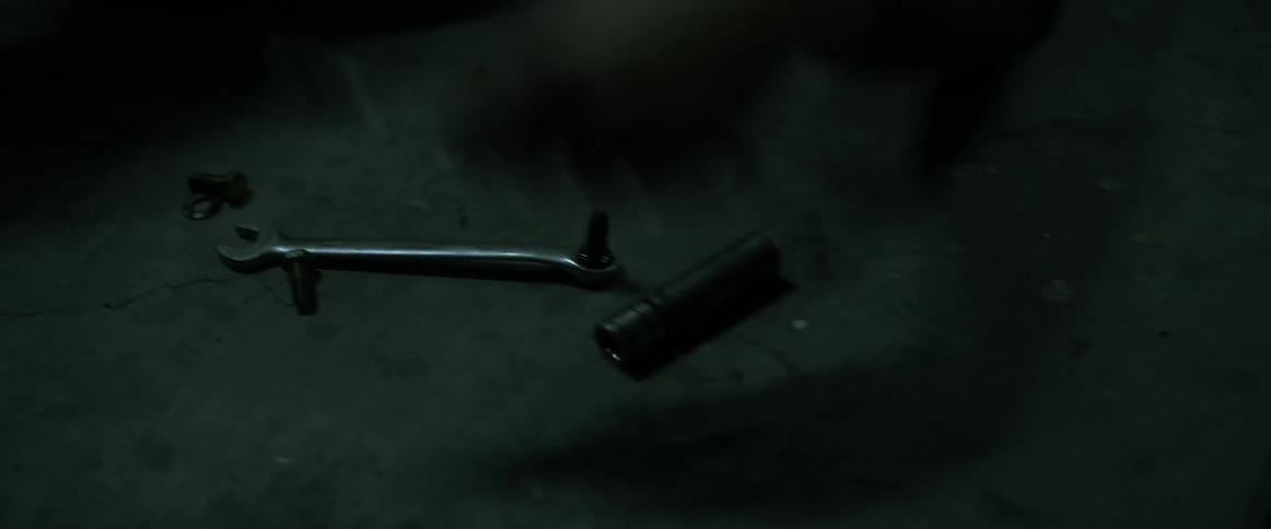 A man in a garage picks up a wrench from the ground