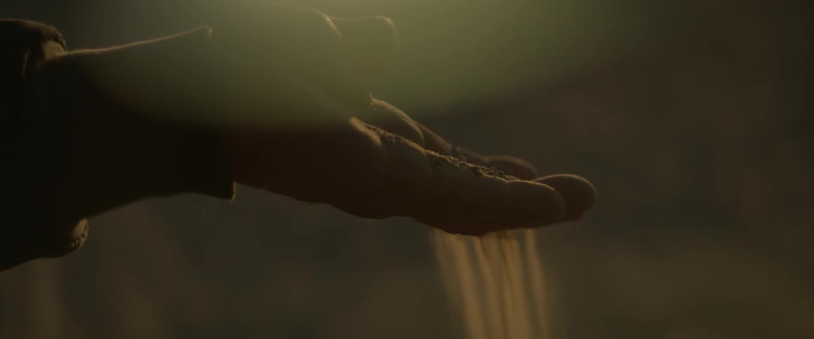 A person sifts sand through their hand into the wind
