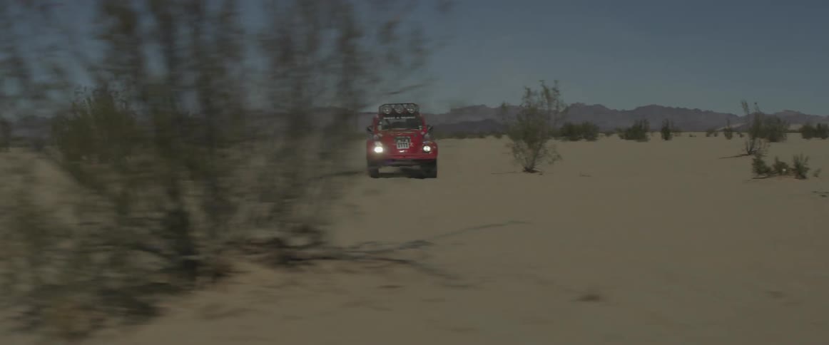 A red car moves quickly over the sand