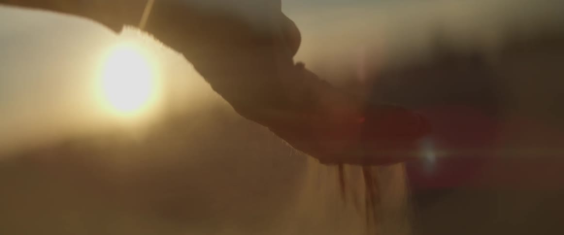 Sand flows through open fingers on a hand at dusk