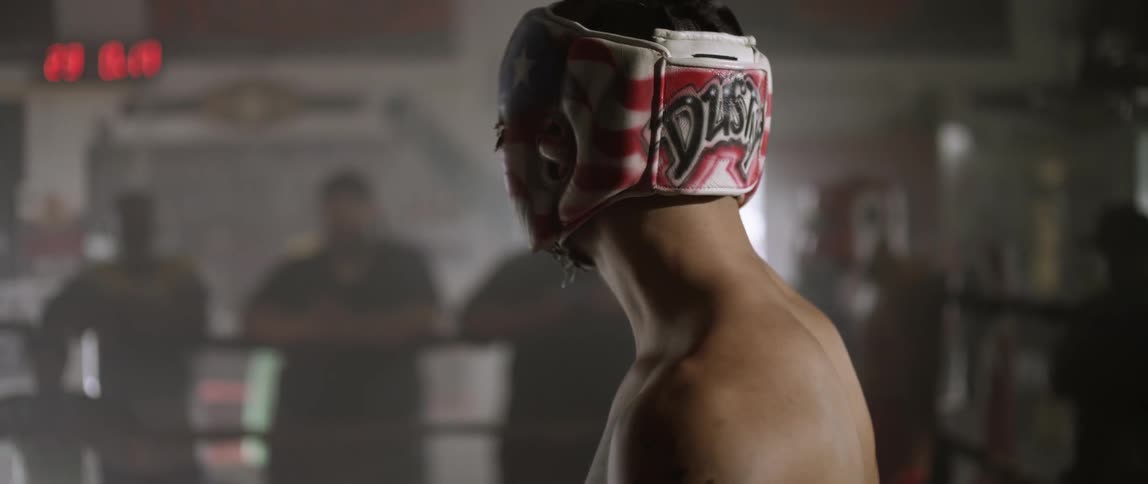 Man wearing headgear turns towards people standing by the ring