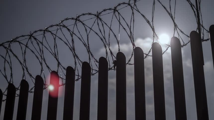 Clouds float over a barbed wire fence