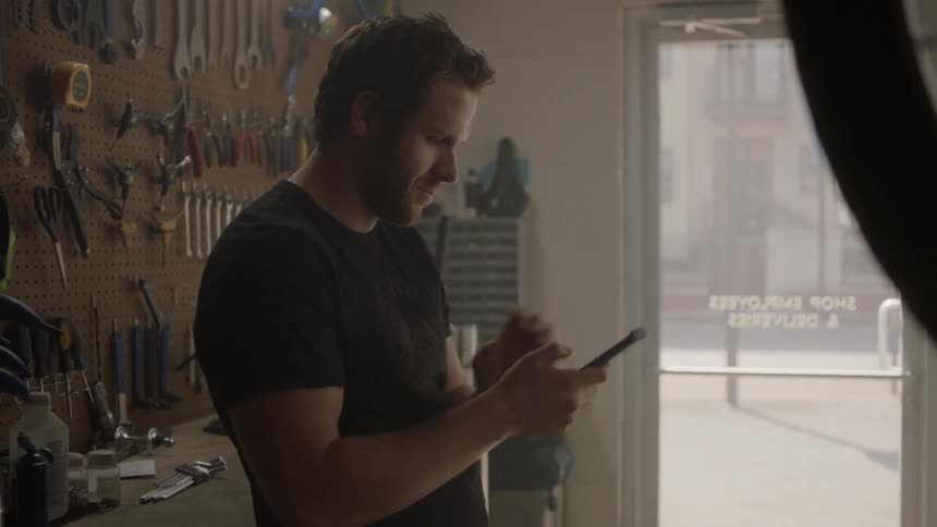 A man is checking his cellphone while he stands in a bike shop