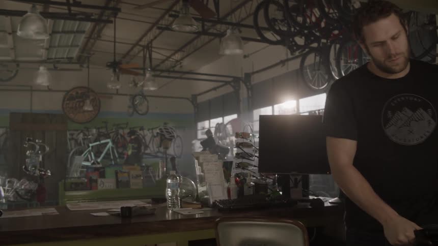 A man guides a bicycle through a bike shop to a repair area in the shop
