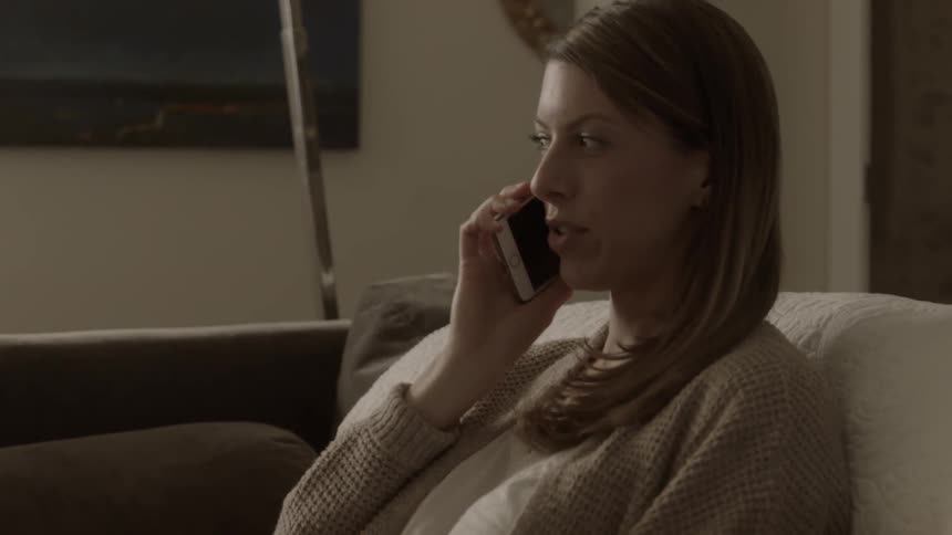 A woman sitting on a couch answers her phone and talks