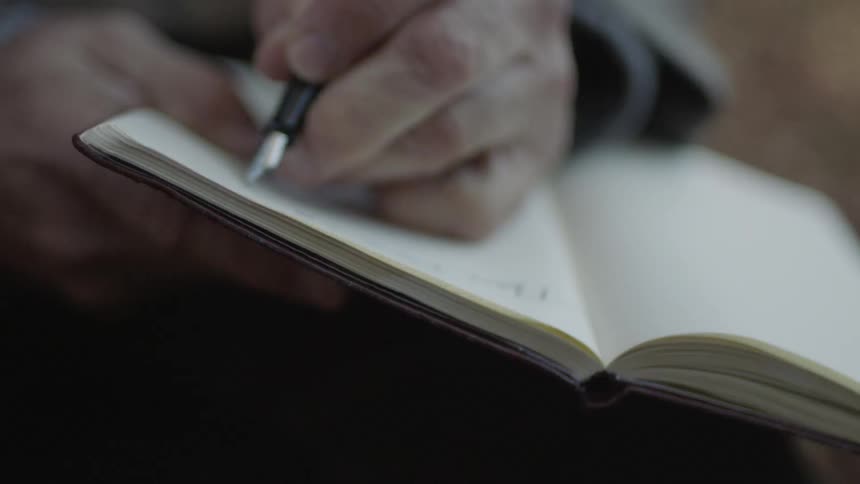 A man writes in a notebook with a pen