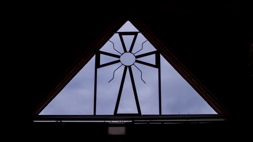 Birds perching and clouds flowing in sky behind window with cross design