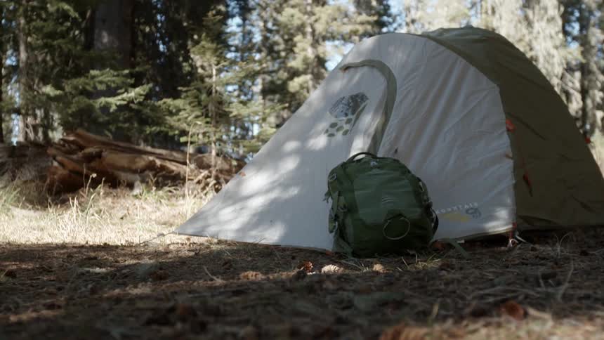 A backpack rests against a tent in the woods