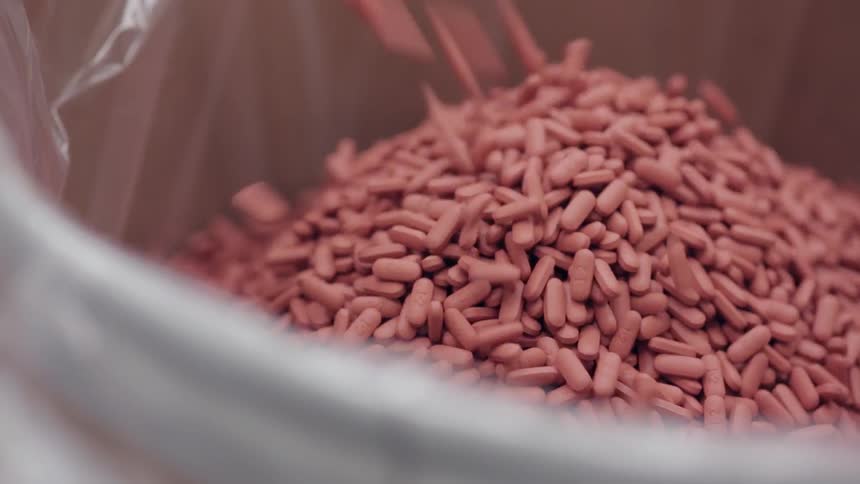 Pills or pellets are pouring into a plastic-lined bin