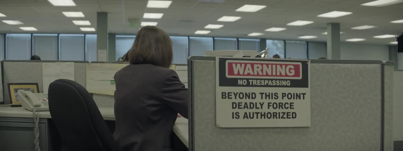 A woman is working in an office cubicle with a 'no trespassing' sign