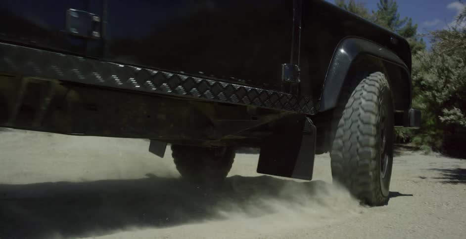 A vehicle drives on a dusty dirt road