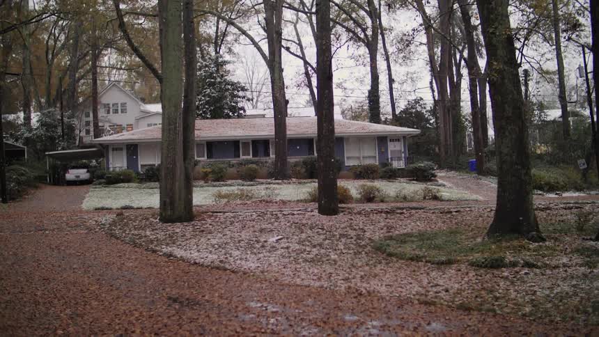 A house with some trees surrounding it and it is snowing