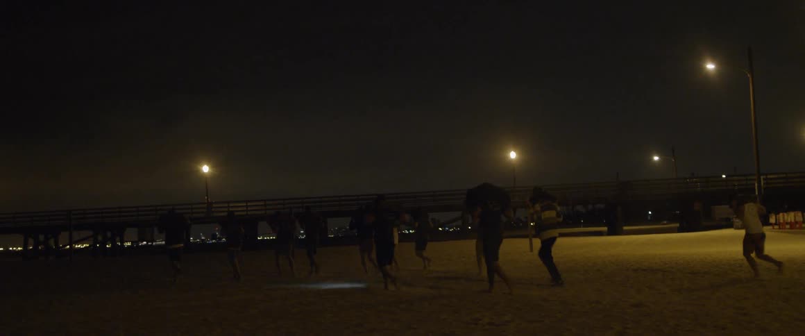 A group of men jog on a beach at night