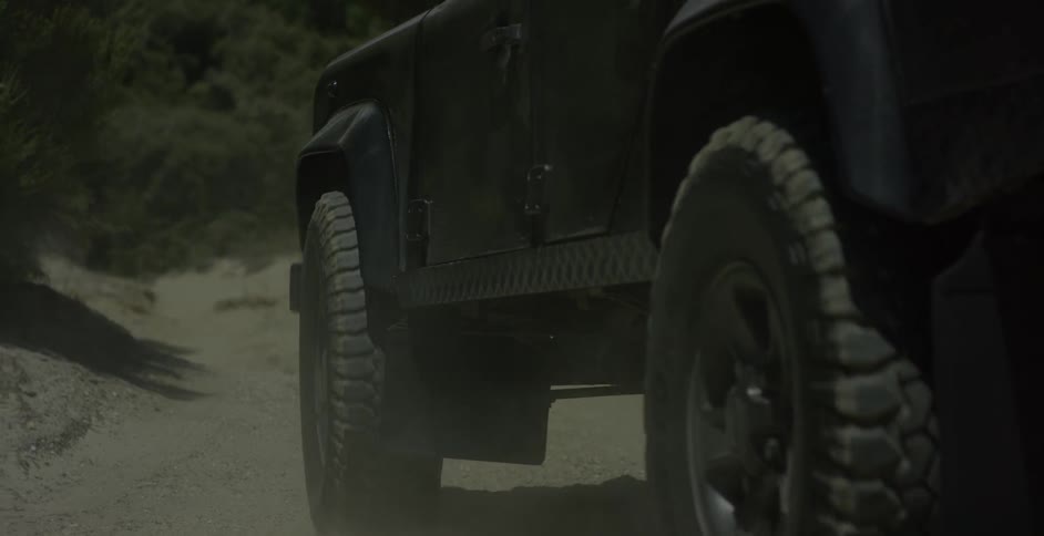 A vehicle drives on a dusty dirt road