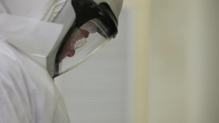 A man in a white safety suit and helmet looks down