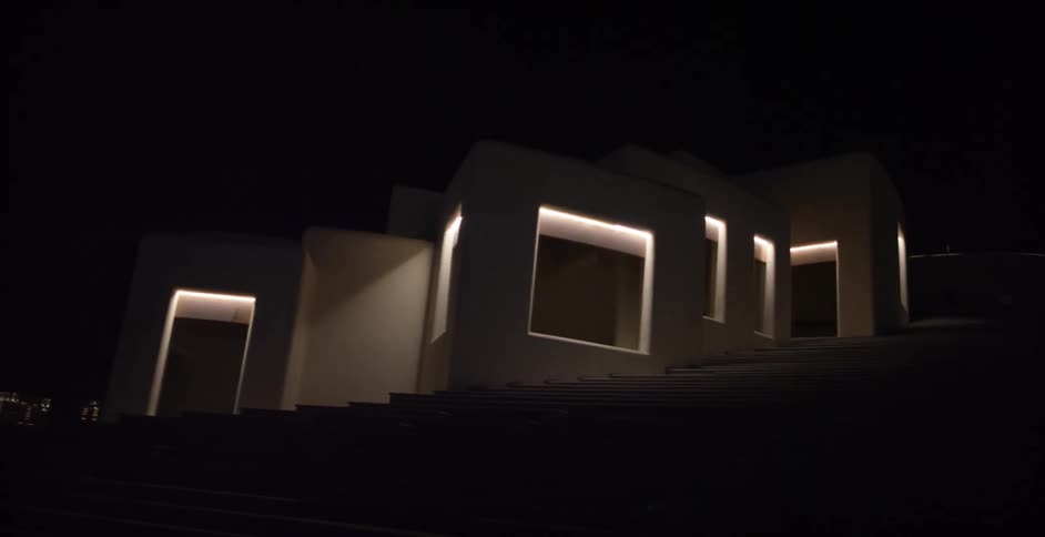 Lights illuminate a building's large windows and doorways
