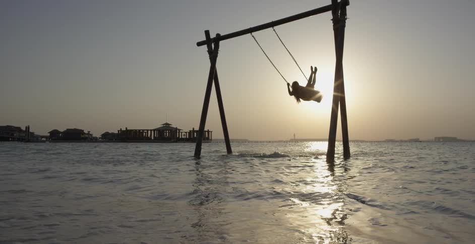 Woman swings on a swing in the ocean water