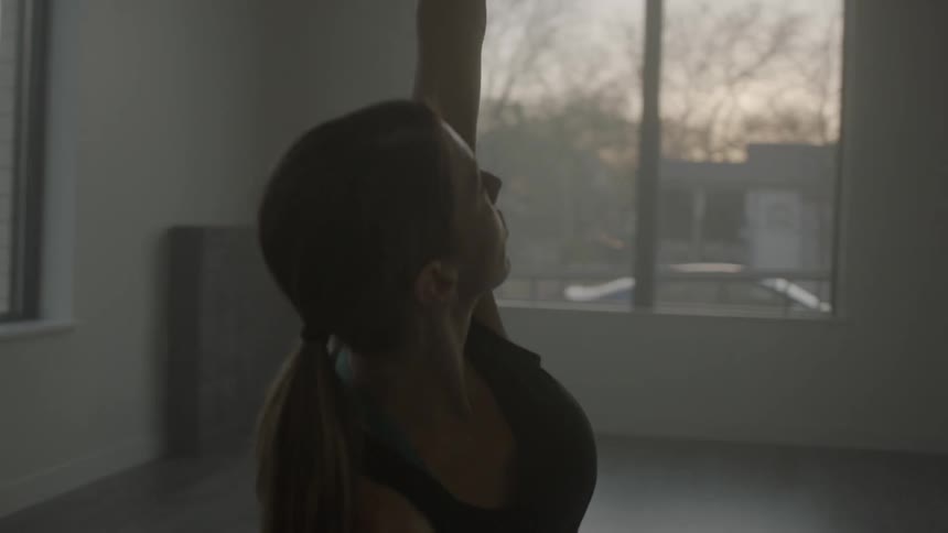 A woman stretches in a room with large windows