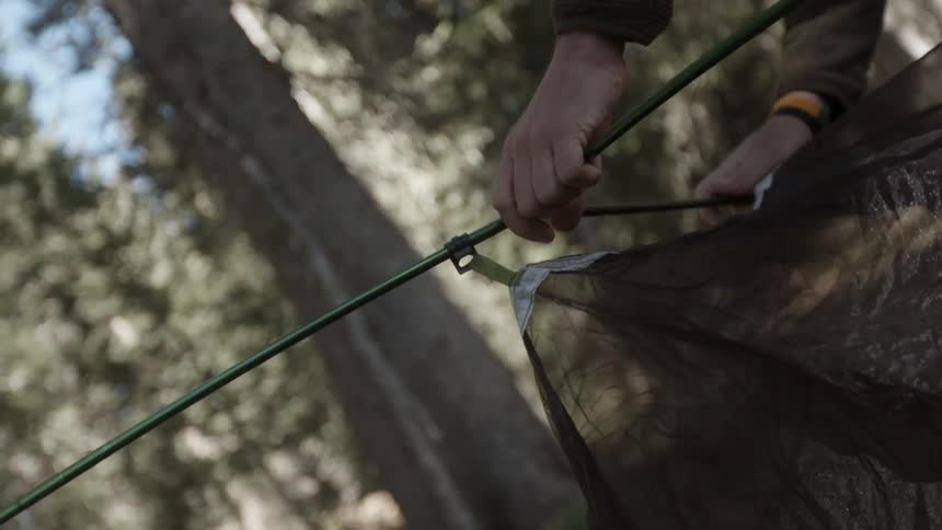 Person assembling a tent in a wooded area
