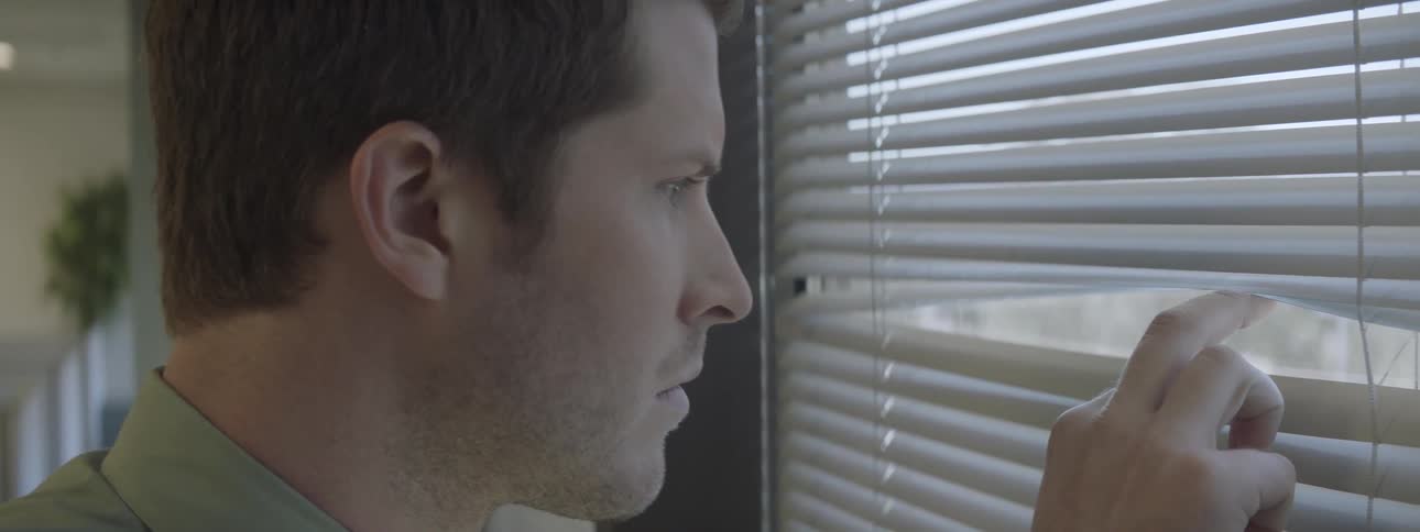 A man peeks through window blinds
