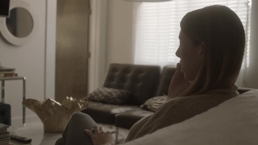 A woman sits on a couch and talks on a phone