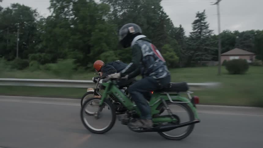 Man passing another while riding mopeds on a paved road