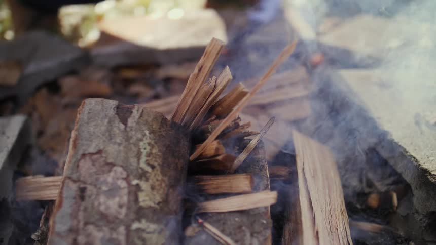 A person adds wood to a smoking campfire