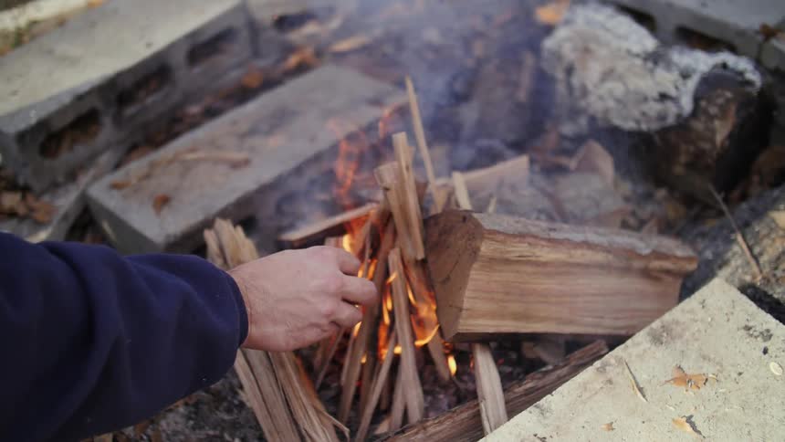 A man adds wood to a burning campfire