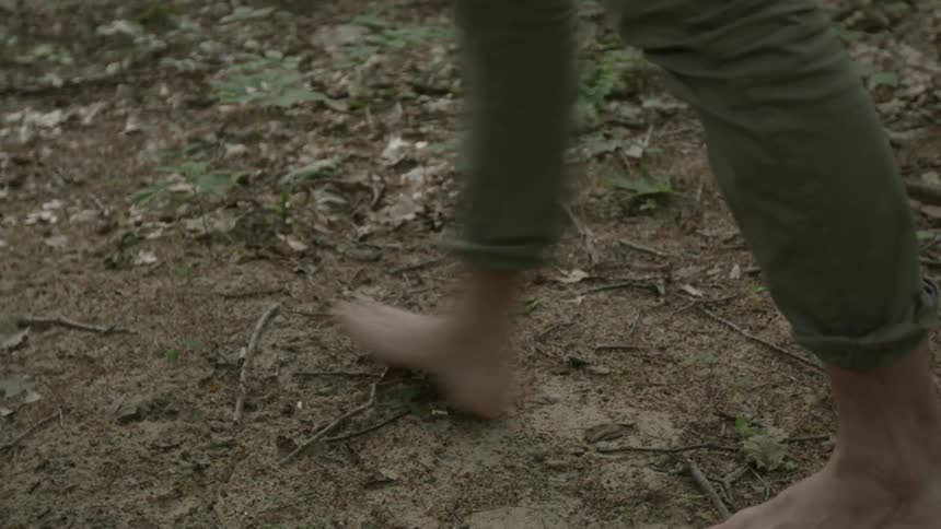 A barefoot man picks up a bundle of firewood