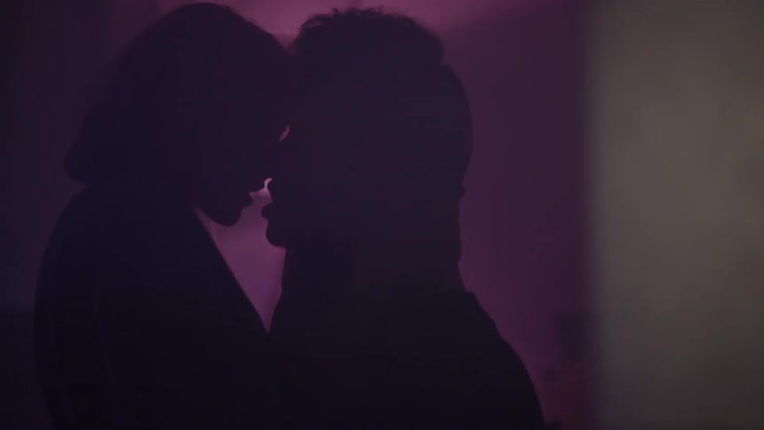 A man and woman kiss with red lights shining around them