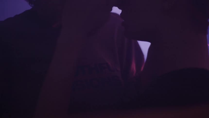 Two people kiss in a dark room with flashing lights and lasers