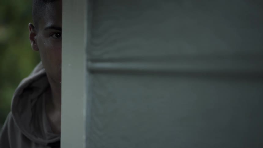 Man peers out from the side of a house