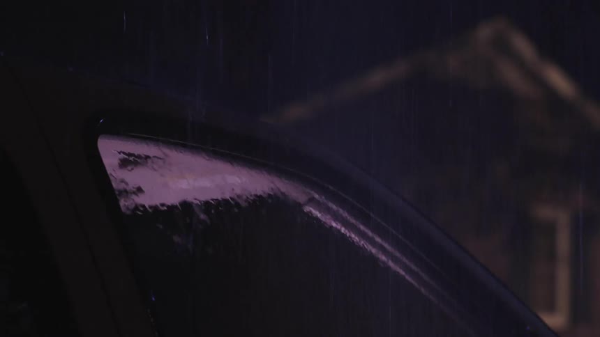 The inside of a car is lit as rain falls on the windows