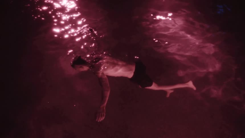 Man floating face down in purple hued water