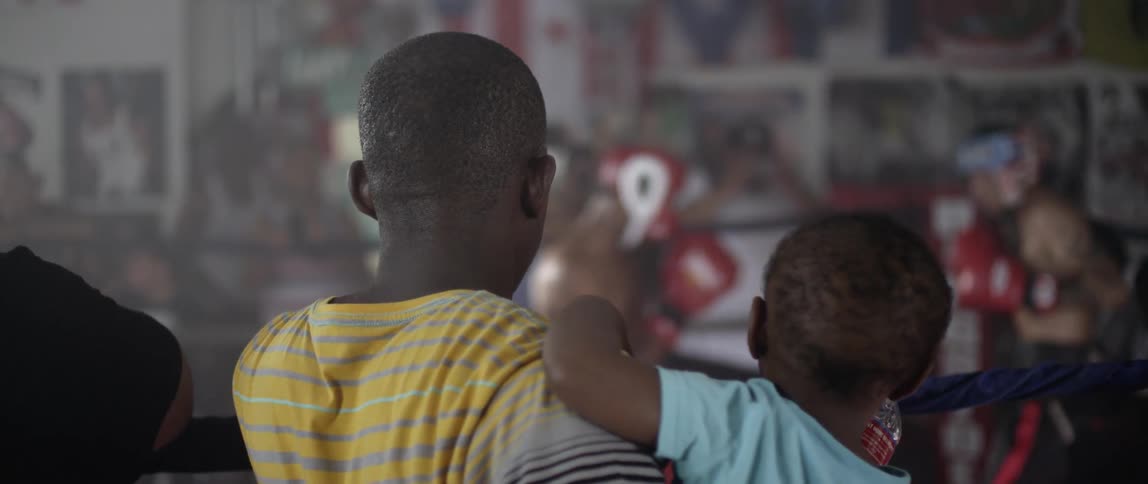 A man holds a toddler while standing ringside while boxers fight
