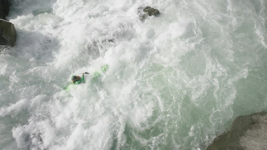 A person struggles to control a kayak in rough river waters