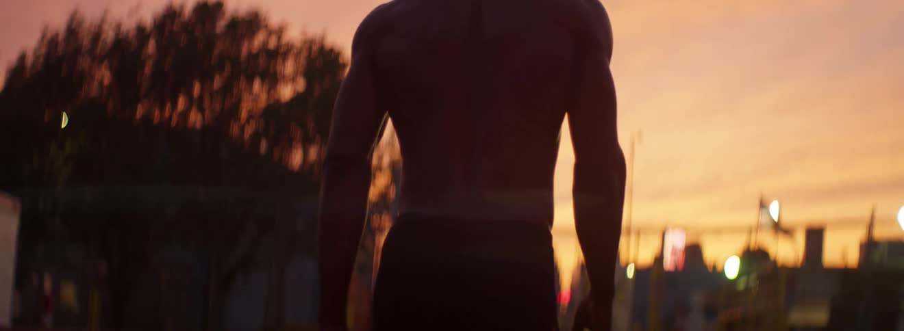 A male athlete is walking down a street at dusk
