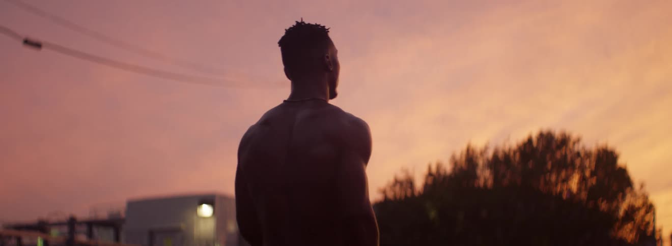 A male athlete walks down the middle of the street at dusk