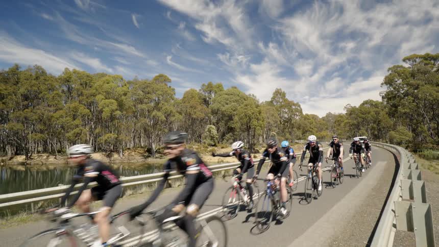 White vehicle follows a group of cyclists down the road