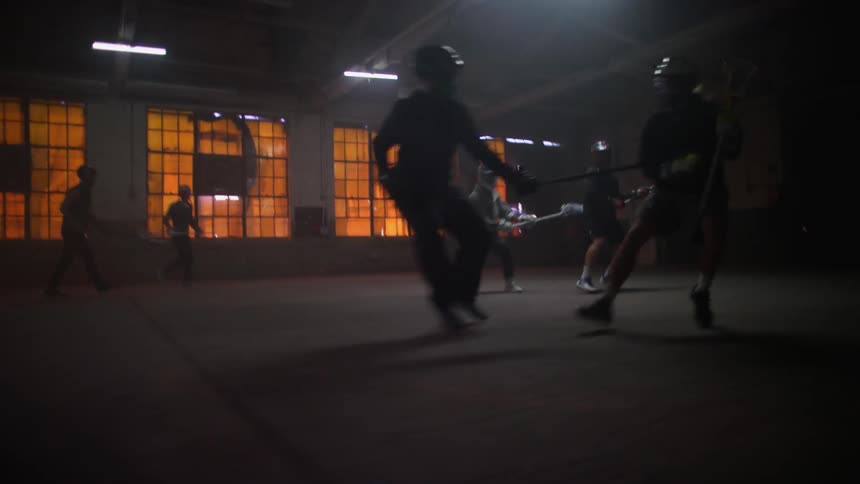 Several people play lacrosse in a dimly lit warehouse
