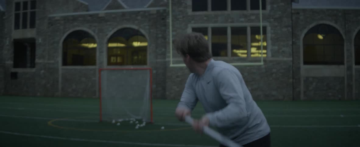 A man scoops up a ball with a net and flings it at a goal net