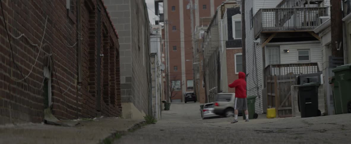 A man is tossing a ball at a wall with a lacrosse stick in an urban area