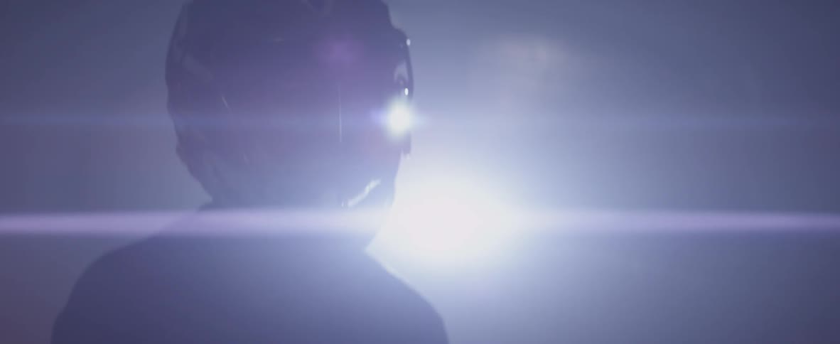 A man wearing a lacrosse helmet moves forward in the dark