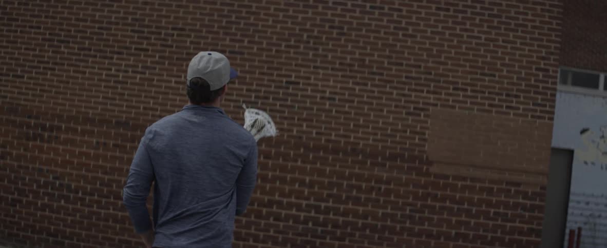 Man throws a ball at a brick wall using a lacrosse stick