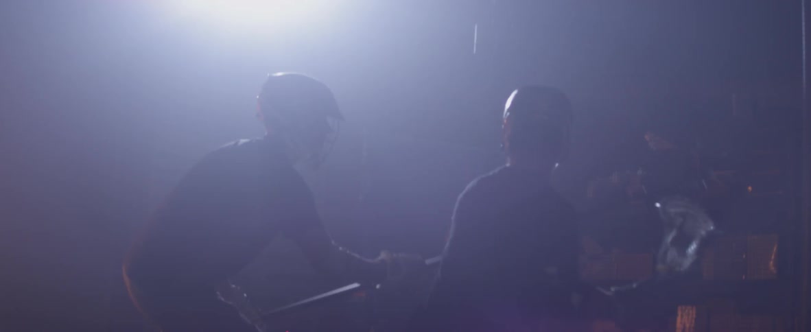 Men play lacrosse in a dark warehouse