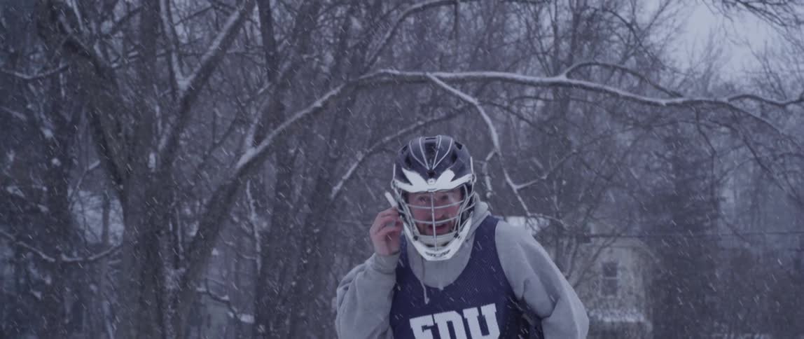 A man plays lacrosse outside while it snows